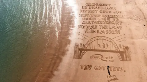 soul2sand/Lines Behind  Beach art shot from a drone looking down on a drawing which reads: "Gan canny be proud, man divent give up! Just keep cannin'. Good luck to all taking part. Howay the lads and lasses! Yiv got this.