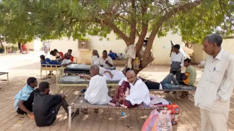 Groups of patients sitting outside hospital on beds and on the floor.