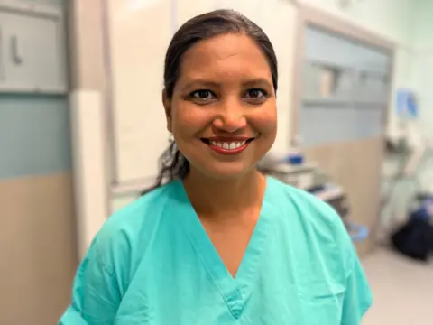 Dr Lucky Saraswat stands in a hospital corridor, wearing bright green scrubs