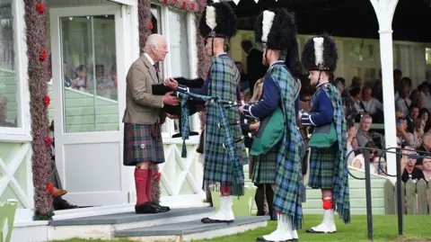 PA Media The King, wearing a kilt, presenting an award