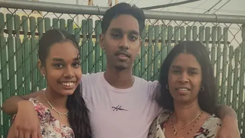 Family Shawn Seesahai with his arms around his sister and mother; they are all smiling at the camera