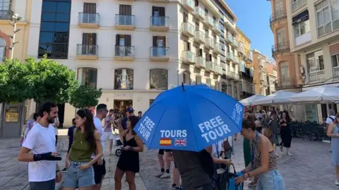 Guy Hedgecoe A tour guide, surrounded by tourists, holds an umbrella 