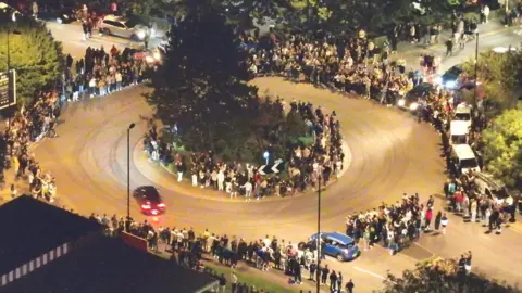 Hampshire Police An overhead shot at night time of cars going around a roundabout whilst crowds line the pavement.