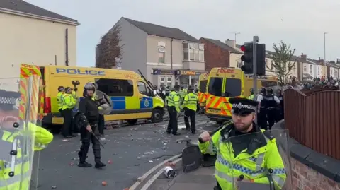 PA Media Riot police holding shields in front of three riot police vans in Southport 