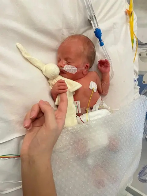 Bradford family Tiny baby Zachary in a hospital cot hooked up to machines and holding his mum or dad's finger