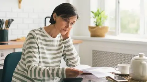 Getty Images A woman staring at a bill in her kitchen