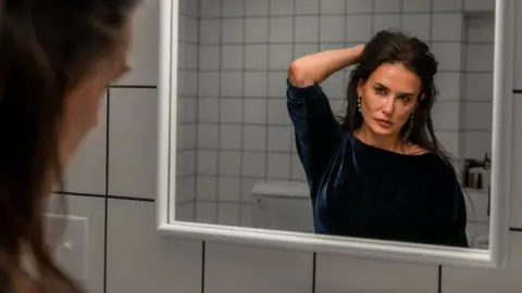 Mubi Demi Moore in The Substance, looking at her face in the mirror