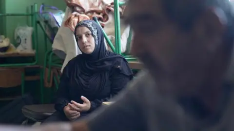 BBC A young woman sits with her hands on her lap, looking pensive