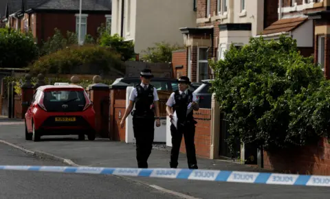 PA Media Two uniformed female police officers walk along Hart Street, close to where the Southport attack happened. A streamer of blue and white police tape is in the foreground of the shot. 