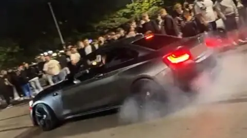 SNAP Footage from the car meet of a black car skidding its tyres in front of a large crowd.