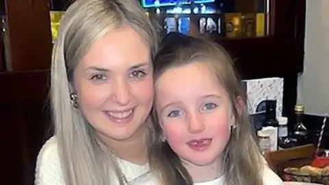 Police Scotland Rebecca Hill in a white jumper with long blonde hair and gold earings, cuddles daughter Arianna, with long hair and two missing front teeth, in a close up photo of their faces