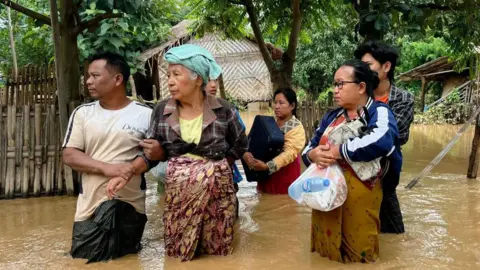 Getty Images Residents stand in flood waters with their belongings in Sin Thay village in Pyinmana, in Myanmar's Naypyidaw region, on September 13, 2024, following heavy rains in the aftermath of Typhoon Yagi. 