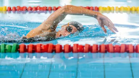 Getty Images A lone female swimmer in a black hat and goggles doing the front crawl