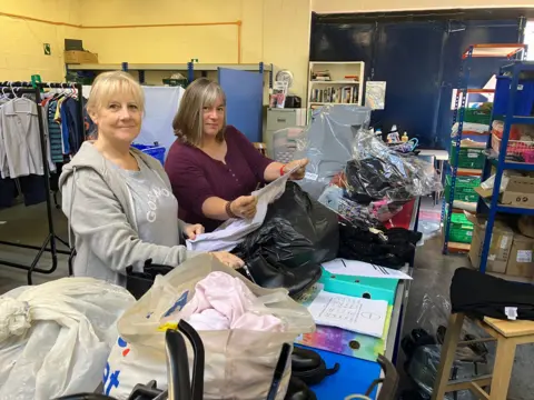 Amy Holmes/BBC A picture of two women, one with blonde hair, the other with brown hair, rummaging through bags of clothes.