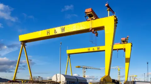 Getty Images Twin shipbuilding gantry cranes in Titanic quarter. They are both yellow with H&W in black lettering printed across the top. The sky is very blue.