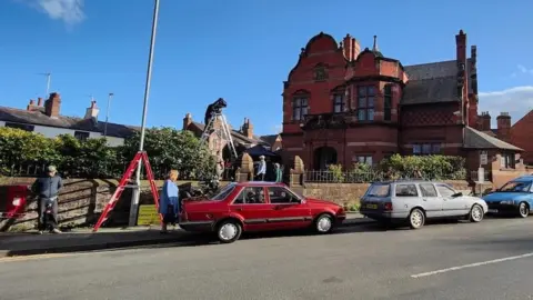 Graham Gordon / Handbridge Life Vintage vehicles are parked along the street outside the old Boys Club on Overleigh Road in Hanbridge. Two ladders, including one with a camera man at the top, can be seen on the road and in the grounds of the club.