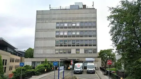 Google Princess Alexandra Eye Pavilion rises five stories high and is a grey building. There are two ambulances in the foreground.