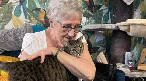 Emma Curtis Susan holding her tabby cat on her lap as she sits on a sofa