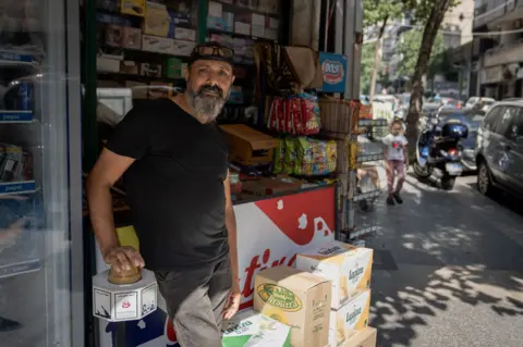 Joel Gunter/BBC Fadi Ali Kiryani outside his Beirut shop. "We will always fly the flag for Hezbollah," he said.