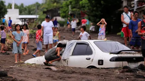 Getty Images Residents look at a car buried by volcanic ash which cascaded into a village triggered by heavy rains brought about by Tropical Storm Trami at a village in Guinobatan town, Albay province South of Manila on October 23, 2024. 