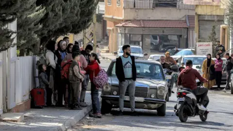 AFP People wait on a road side for a lift after the Israeli military issued evacuation orders covering the entire city of Baalbek, in the Bekaa Valley, eastern Lebanon (30 October 2024)