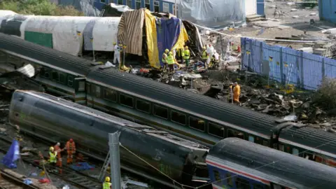 Getty Images The debris from the crash with rail workers in high vis jackets and hard hats on the track