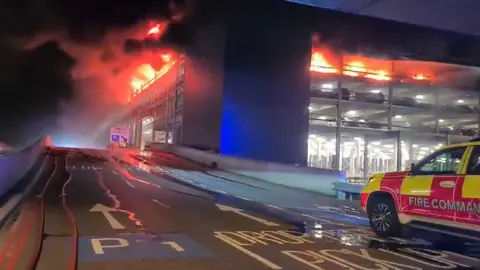 PA Media A fire command vehicle is parked close to the burning car park building