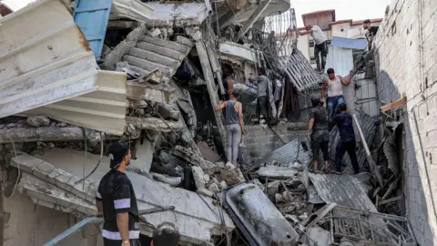 AFP Palestinians attempt to rescue a man trapped underneath the remains of a building hit by Israeli bombardment, in the Saftawi district of Jabalia, in the northern Gaza Strip (15 October 2024)