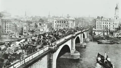 The London Archives, City of London A black and white photograph from 1895 showing horse-drawn traffic on the original London Bridge