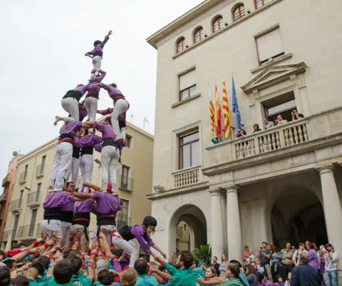 Peter Norris People dressed in purple and white are boosted on top of each other to form a tower 