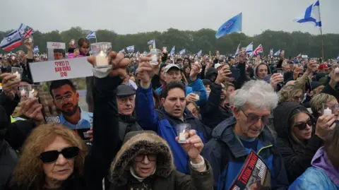 PA Media Memorial attendees hold pictures of hostages, candles and wave Israeli flags