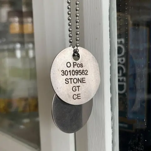 Kevin Shoesmith/BBC News Dog tags belonging to Private Gregg Stone. Stamped on a round metal disc, attached to a chain necklace, are the words O Pos (his blood group), 30109562 (his Army number), Stone GT, CE (for Church of England).