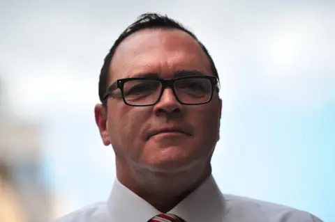 Getty Christopher Ciccone pictured in 2012 with short black hair, black glasses, and a white shirt with a red and grey striped tie