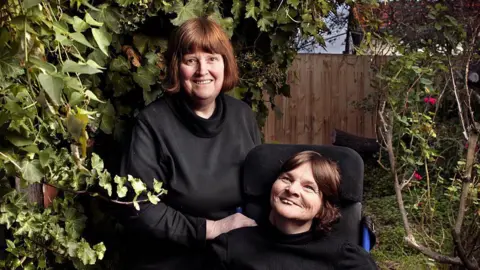 Getty Images Rosemary Crossley, wearing a dark top and looking straight at the camera, and Anne McDonald in a wheelchair. The picture appears to be professionally taken and they are in a back garden.