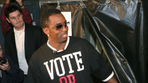 Getty Images Sean "Diddy" Combs is photographed with a voting T-shirt at an event in 2004 urging others to vote in the election. In the background, his publicist Rob Shuter appears. 