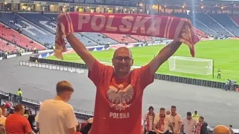 Facebook Jaroslaw Rossa at a football match holds a Polska scarf over his head.