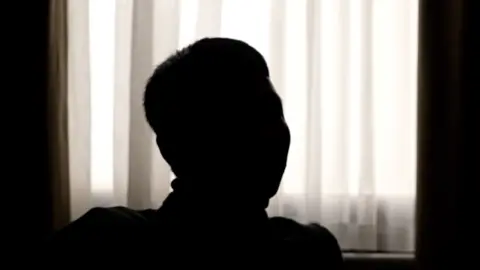 A black silhouette of man - head and shoulders. Behind him is a white curtain. 