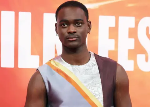 EPA Ethan Herisse poses on the red carpet for the Nickel Boys gala screening at the BFI London Film Festival - he is wearing a silver, yellow, white and brown silk and lace sleeveless top.