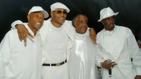 Getty Images Sean "Diddy" Combs poses for a photo with music producer Russell Simmons, rapper LL Cool J and Rev Al Sharpton. All are wearing white 