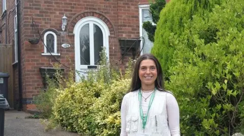 Claudia Bowring standing in front of some bushes and an abandoned house