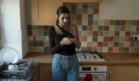 Stacey leaning on a kitchen counter looking at her mobile phone