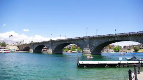 Cal Sheehy A modern-day image of the original bridge in Lake Havasu, Arizona - with US flags, a boat and a water scooter visible on the water 