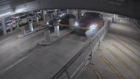 Bedfordshire Fire and Rescue Service CCTV footage of inside the car park, a red Range Rover Sport is parked at the entry barrier a small amount of light smoke is emitting from the engine and covering a headlight