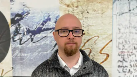 Adam Murray wearing glasses and a grey woolen sweater 