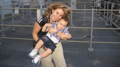 William McCulloch/PA  Nadia Ayoub McCullough outdoors with her son Thomas, pictured as a toddler. She is standing and holding him in front of her.