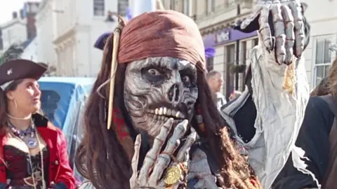 James Lacey A person posing for the camera wearing a skeleton mask and pirate headband with dreadlocked hair