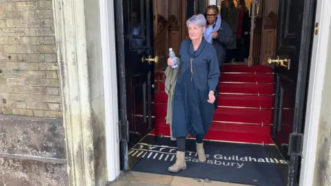 Caroline Sturgess wears a navy blue dress. She is walking out of Salisbury Guildhall