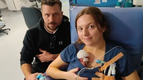 Family photo Daniel and Chantelle sitting with Robyn in hospital. Robyn is tiny, the size of her mum's hand as she snuggles into her chest. 