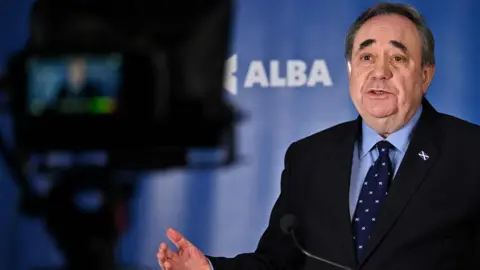 Getty Images Alex Salmond standing behind a TV camera with the Alba logo visible in the background