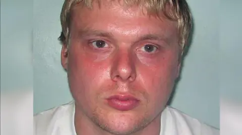 Metropolitan Police Steven Barker police mugshot image. He looks towards the camera and has a sweaty pink face, blond hair and is unshaven